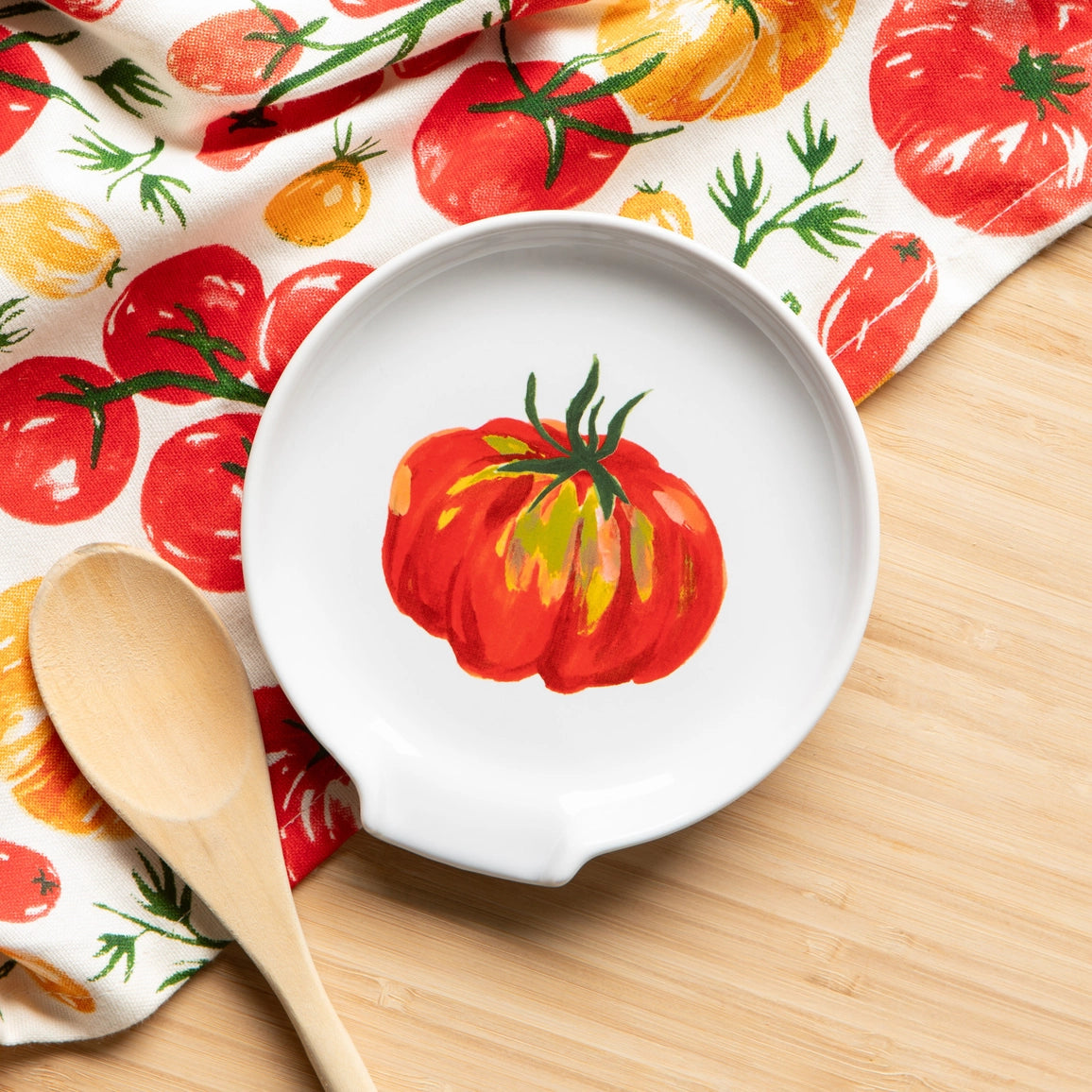White plate with tomato design on a wooden table with a matching towel in the background.