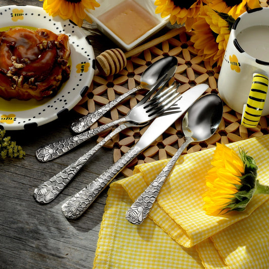 Silver cutlery set on a wooden table with yellow napkins and sunflowers.
