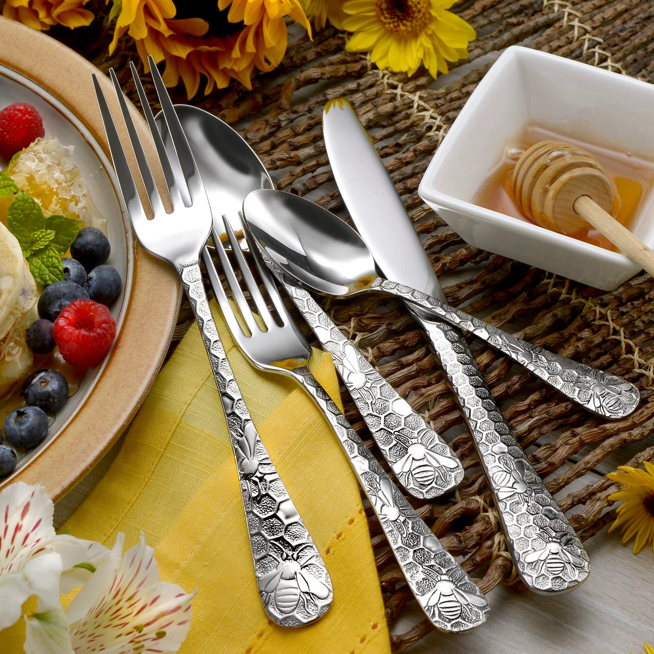 Silver cutlery set on a table with a plate of fruit and a small bowl of honey.