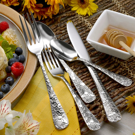 Silver cutlery set on a table with a plate of fruit and a small bowl of honey.
