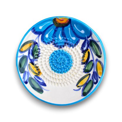 A round white ceramic plate with a vibrant blue floral hand-painted design, featuring blue, green, yellow, and orange accents on a white background.
