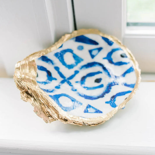 Decorative dish with blue geometric pattern inside a gold-rimmed shell on a white surface.