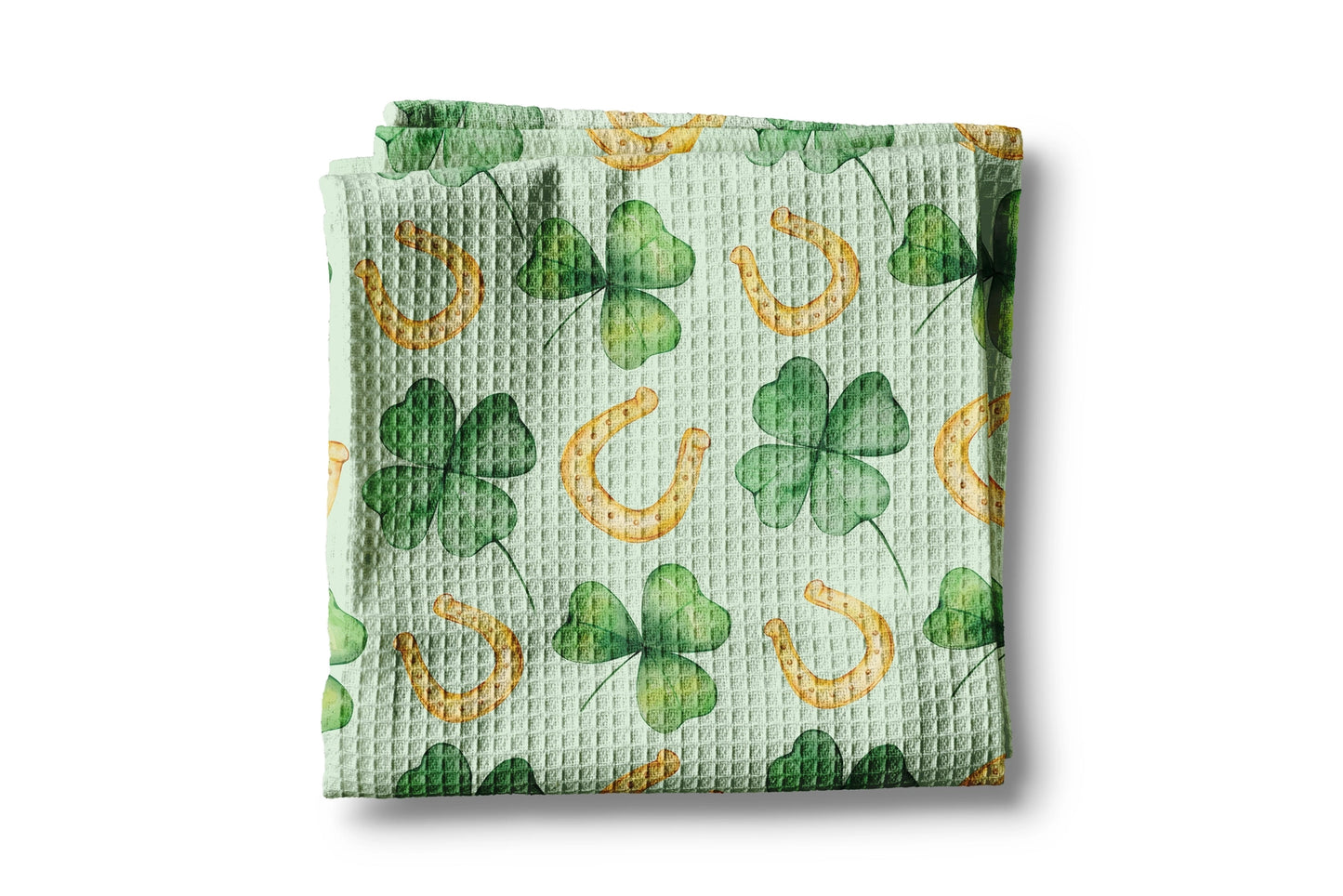 Green waffle-textured towel with clover and horseshoe pattern on a white background