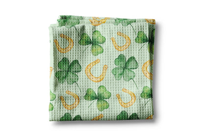 Green waffle-textured towel with clover and horseshoe pattern on a white background