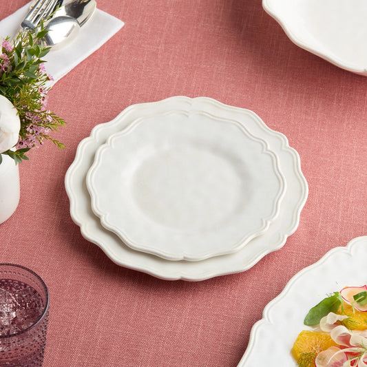 Stack of white ceramic plates on a pink tablecloth with floral decorations.