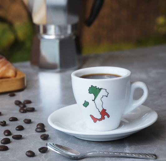 White coffee cup with Italian map design on a saucer, surrounded by coffee beans and a spoon on a wooden surface.
