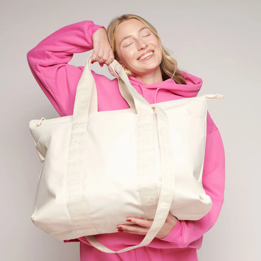 Person wearing a pink hoodie holding a large white tote bag against a plain background