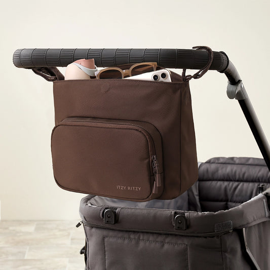 Brown stroller organizer attached to a stroller with sunglasses and a phone inside.