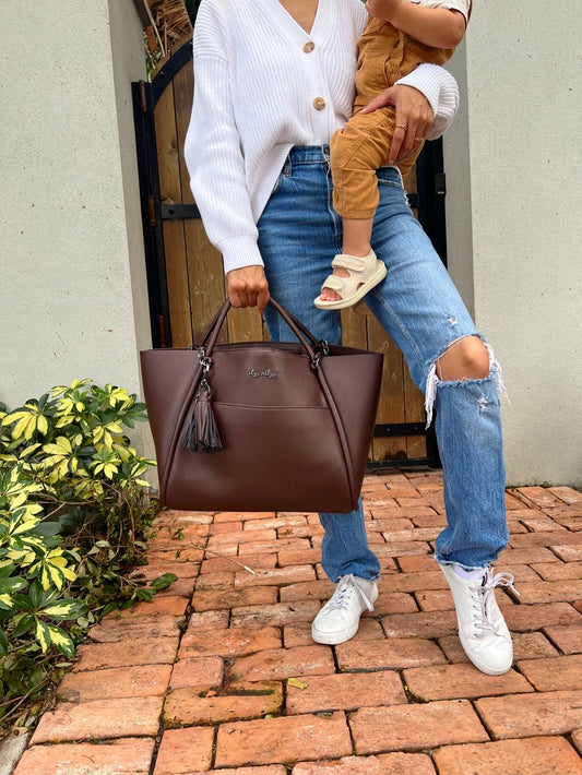 Woman holding a child and a brown handbag on a brick path.