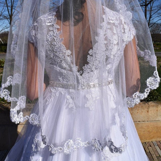Person wearing a white lace Communion dress with a matching veil.