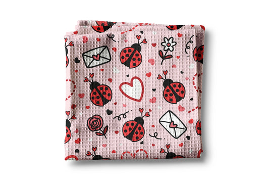 Folded pink blanket with ladybug and heart patterns on a white background