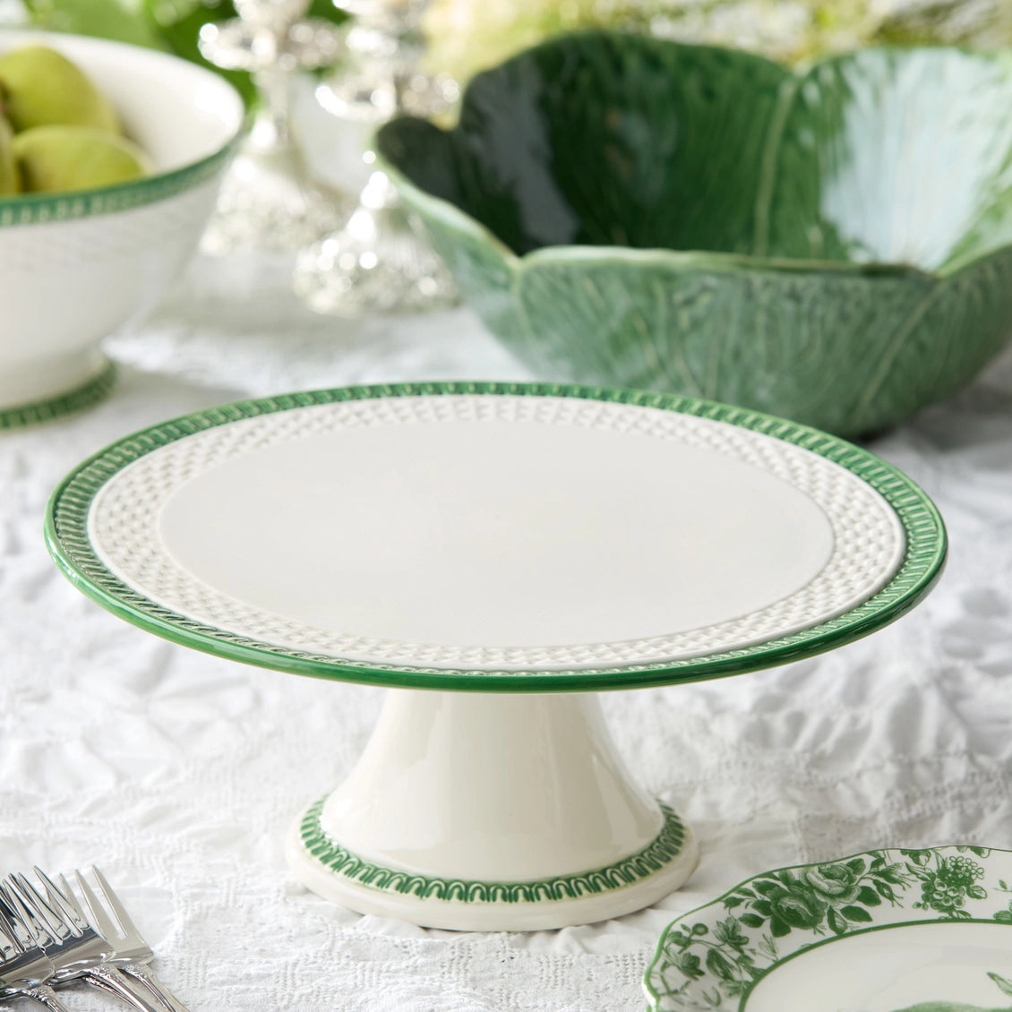 White cake stand with green decorative edge on a table setting.