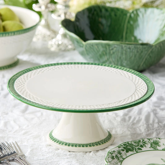 White cake stand with green decorative edge on a table setting.