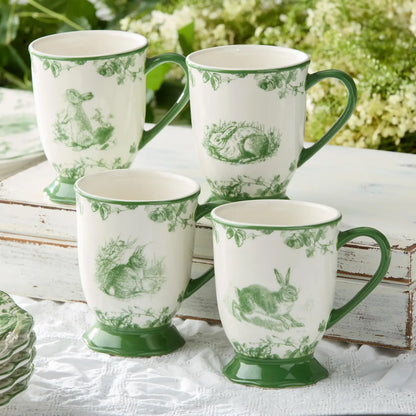 Set of four white mugs with green floral patterns on a white surface with greenery in the background.