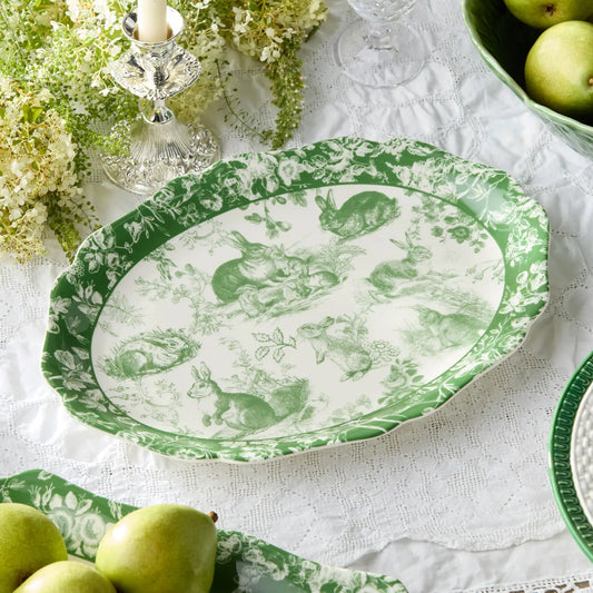 Green and white patterned plate on a table with pears and flowers