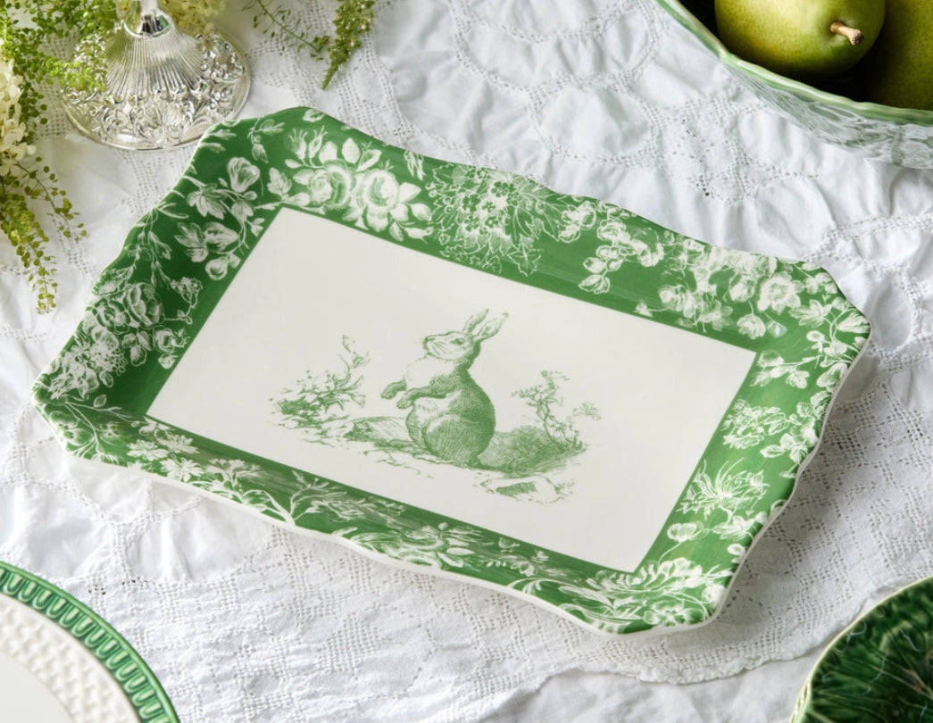 Green and white decorative tray with a rabbit design on a tablecloth with green apples.