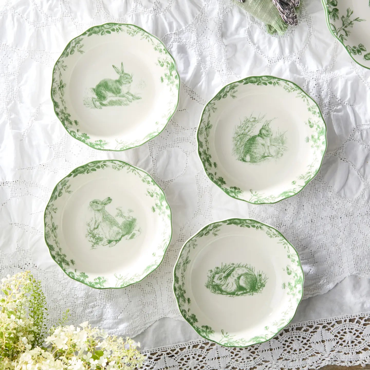 Set of white plates with green rabbit illustrations on a lace tablecloth.