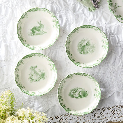 Set of white plates with green rabbit illustrations on a lace tablecloth.