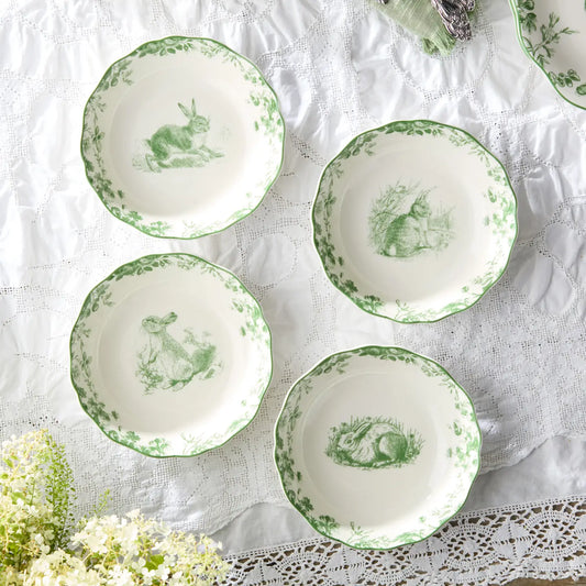 Set of white plates with green rabbit illustrations on a lace tablecloth.