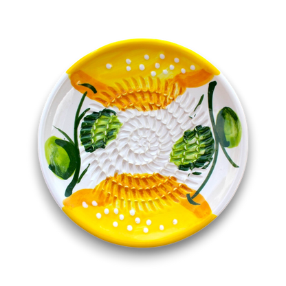 A round white ceramic plate with a hand-painted yellow and green floral pattern, featuring textured yellow sections with white dots and green leaf motifs, shown on a white background.