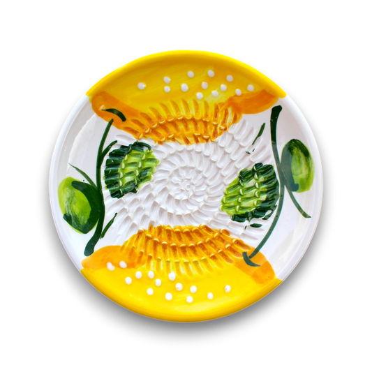 A round white ceramic plate with a hand-painted yellow and green floral pattern, featuring textured yellow sections with white dots and green leaf motifs, shown on a white background.