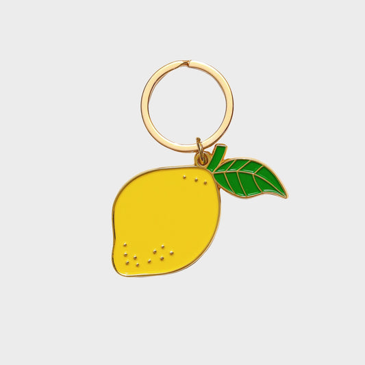 Gold keychain with a yellow lemon and green leaf on a light gray background