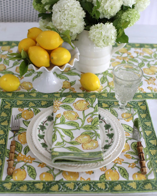 Table setting with lemons, flowers, and patterned tablecloth on a white surface