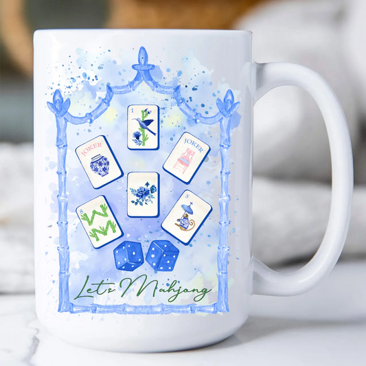 A white ceramic mug featuring a blue watercolor-style illustration of a bamboo frame with six playing cards and two dice, plus the text 'Let's Mahjong' in green script.