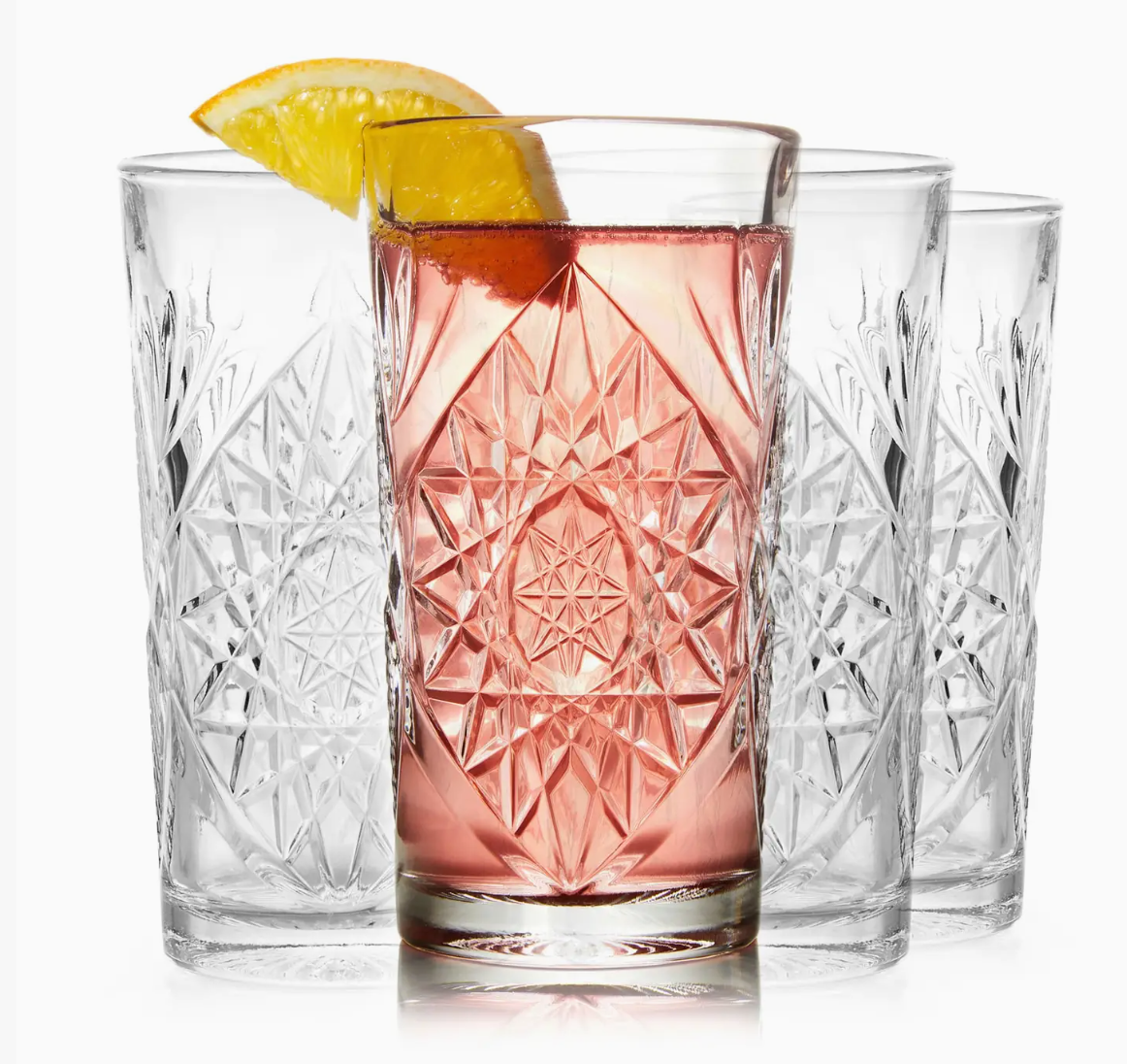 Set of four crystal glasses with a pink drink and lemon slices on a white background