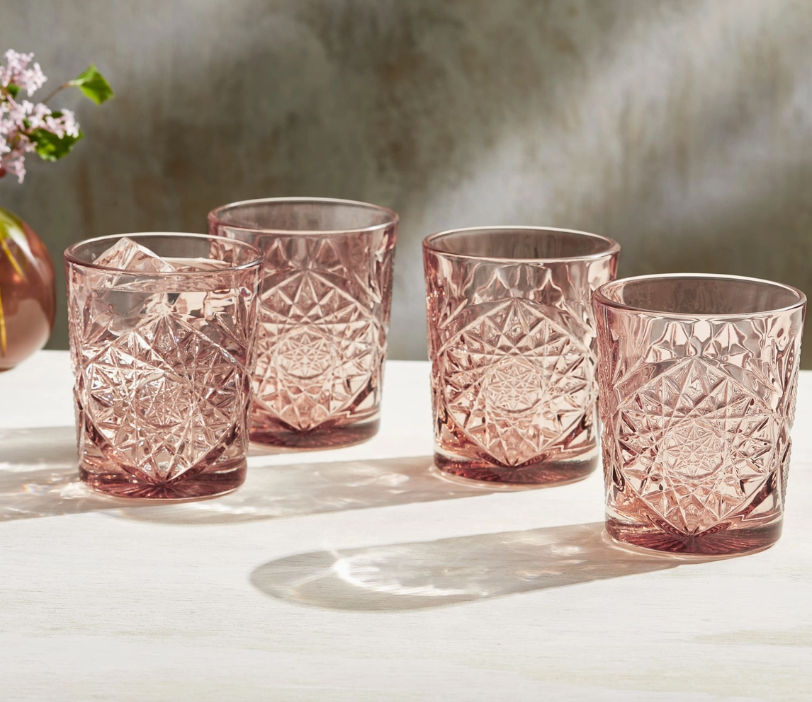 Set of four pink glass tumblers with textured design on a light surface.