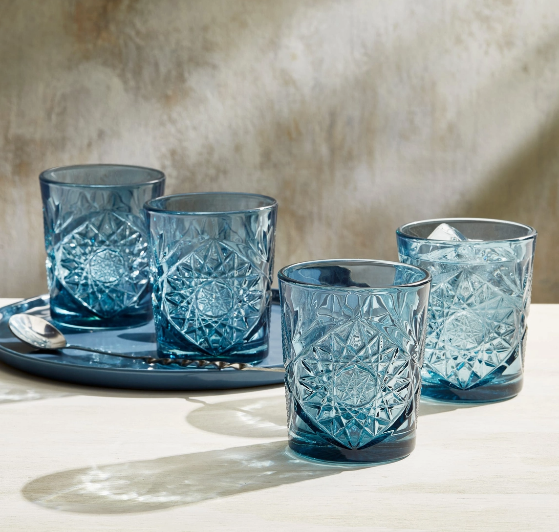 Set of four blue glass tumblers with textured design on a tray against a neutral background