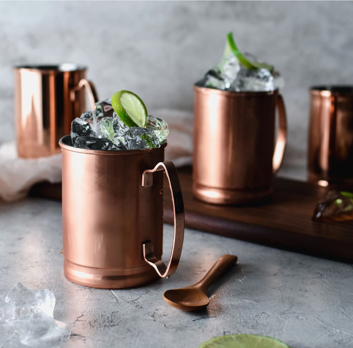 Copper mugs with drinks garnished with lime wedges on a stone surface.