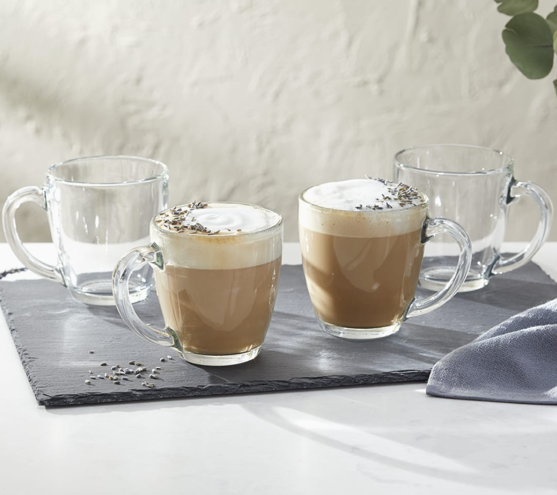 Four glass mugs with hot beverages on a slate tray against a neutral background