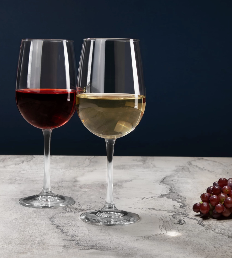 Two wine glasses with red and white wine on a marble surface with grapes.