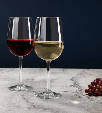 Two wine glasses with red and white wine on a marble surface with grapes.