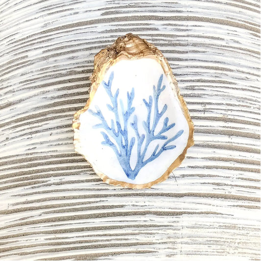 Decorative oyster shell dish with blue coral design on a textured surface