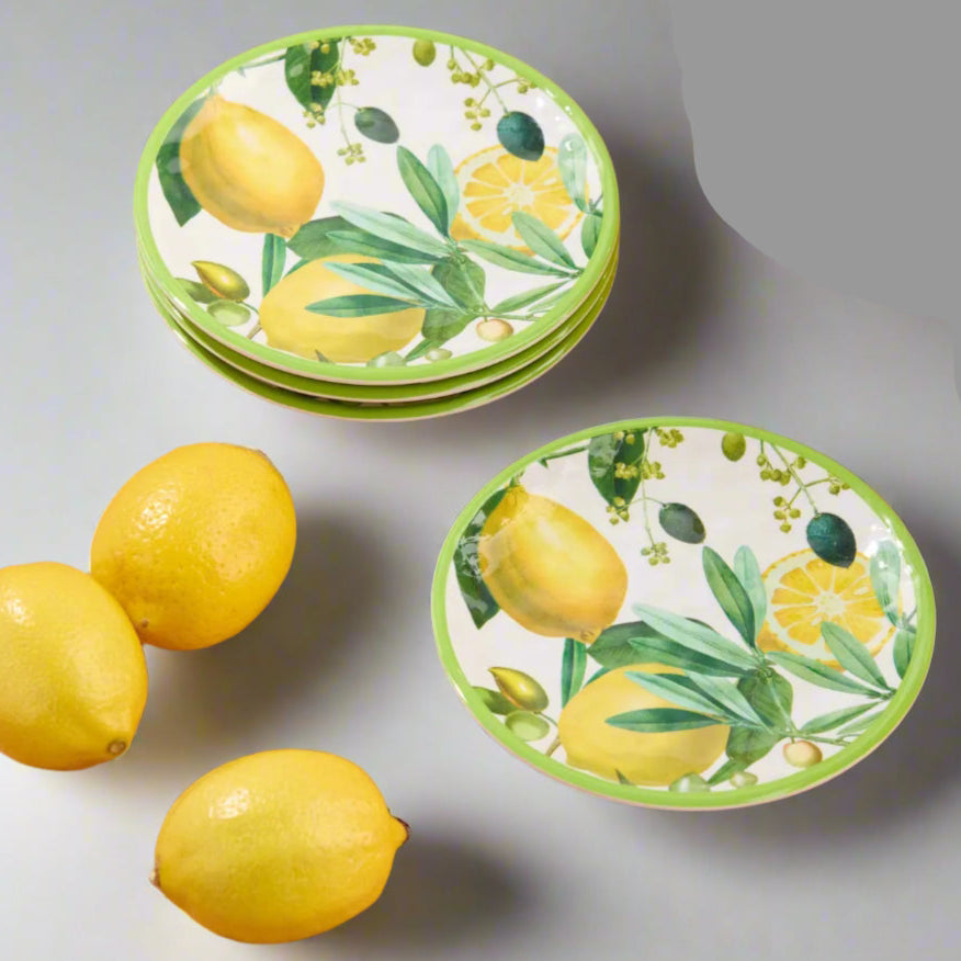 Set of ceramic plates with lemon design on a terracotta surface with lemons and a teapot.