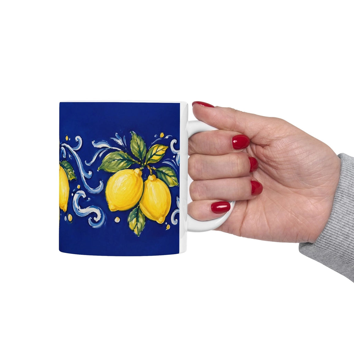 A hand with red nail polish holds a white ceramic mug featuring a dark blue background decorated with yellow lemons, green leaves, and white decorative swirls.