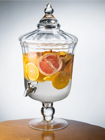 Glass beverage dispenser with fruits on a wooden surface