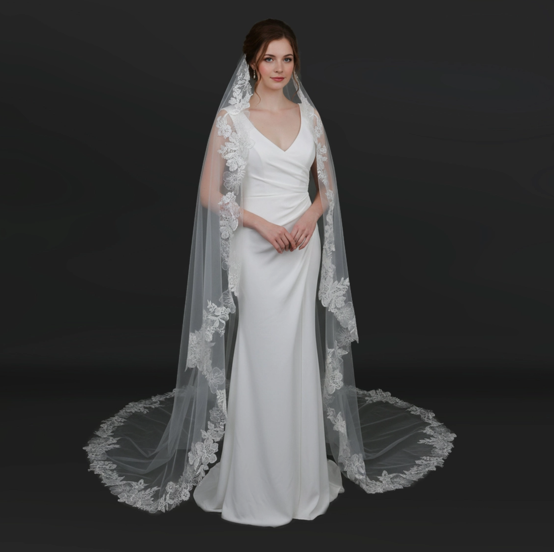Woman wearing a white wedding dress with a long lace veil on a black background