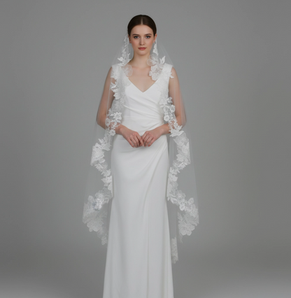 White wedding dress with floral lace capelet on a gray background