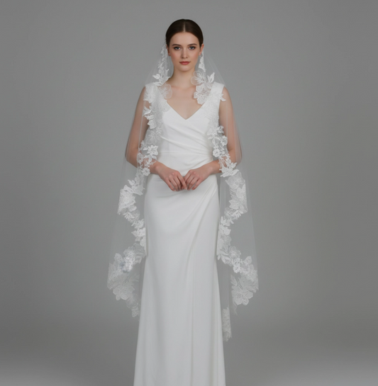 White wedding dress with floral lace capelet on a gray background