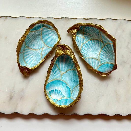 Three decorative shell-shaped bowls with gold edges and blue interior on a marble surface