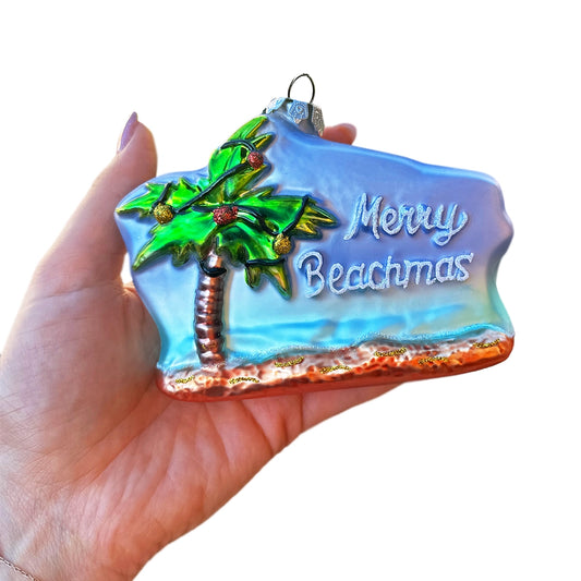 Decorative ornament with palm tree and 'Merry Beachmas' text held in a hand.