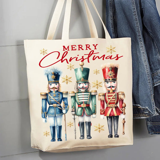 A cream canvas tote bag with a 'Merry Christmas' nutcracker print, hanging next to a blue denim jacket against a gray paneled wall.