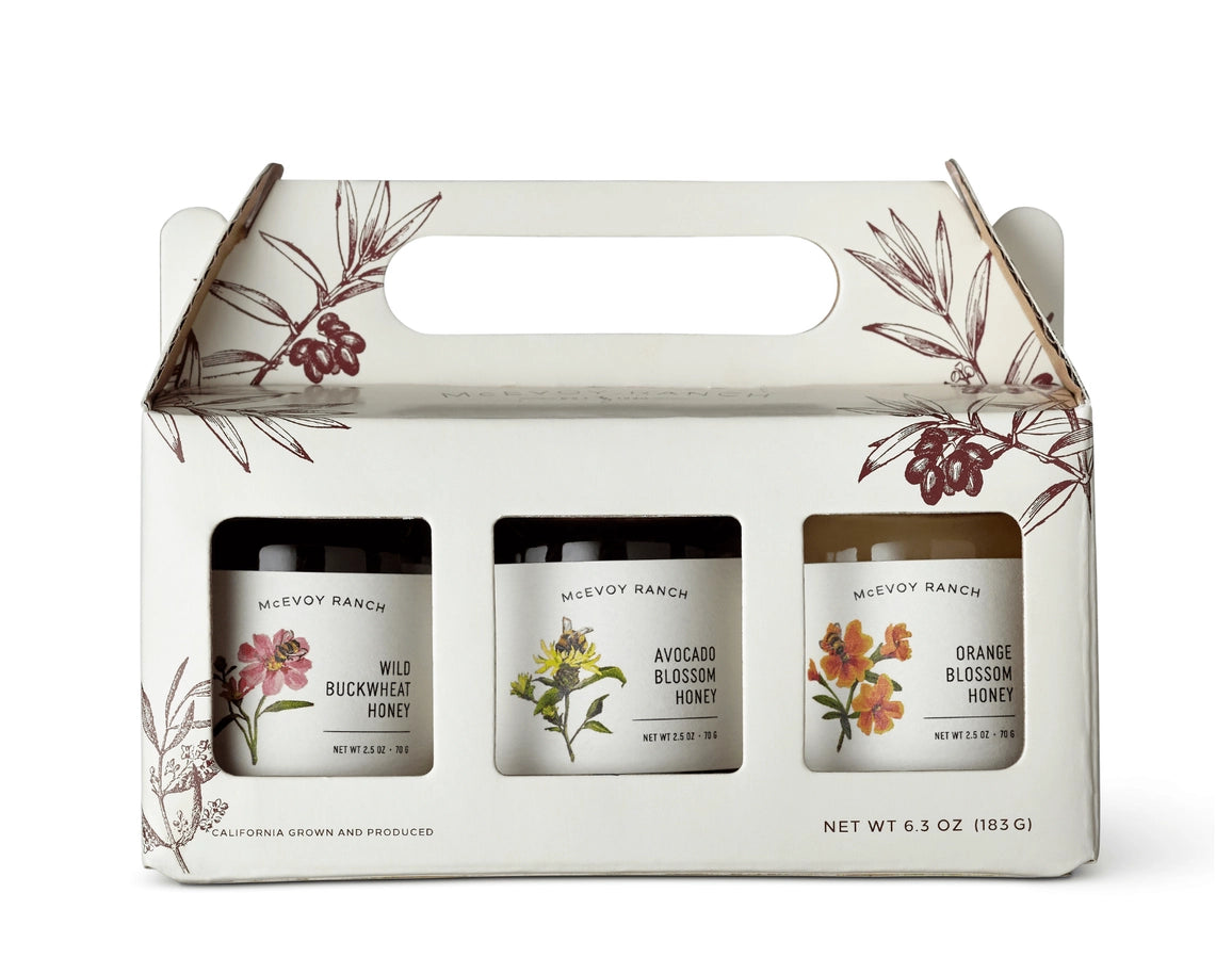 Three honey jars in a decorative box with floral designs on a white background