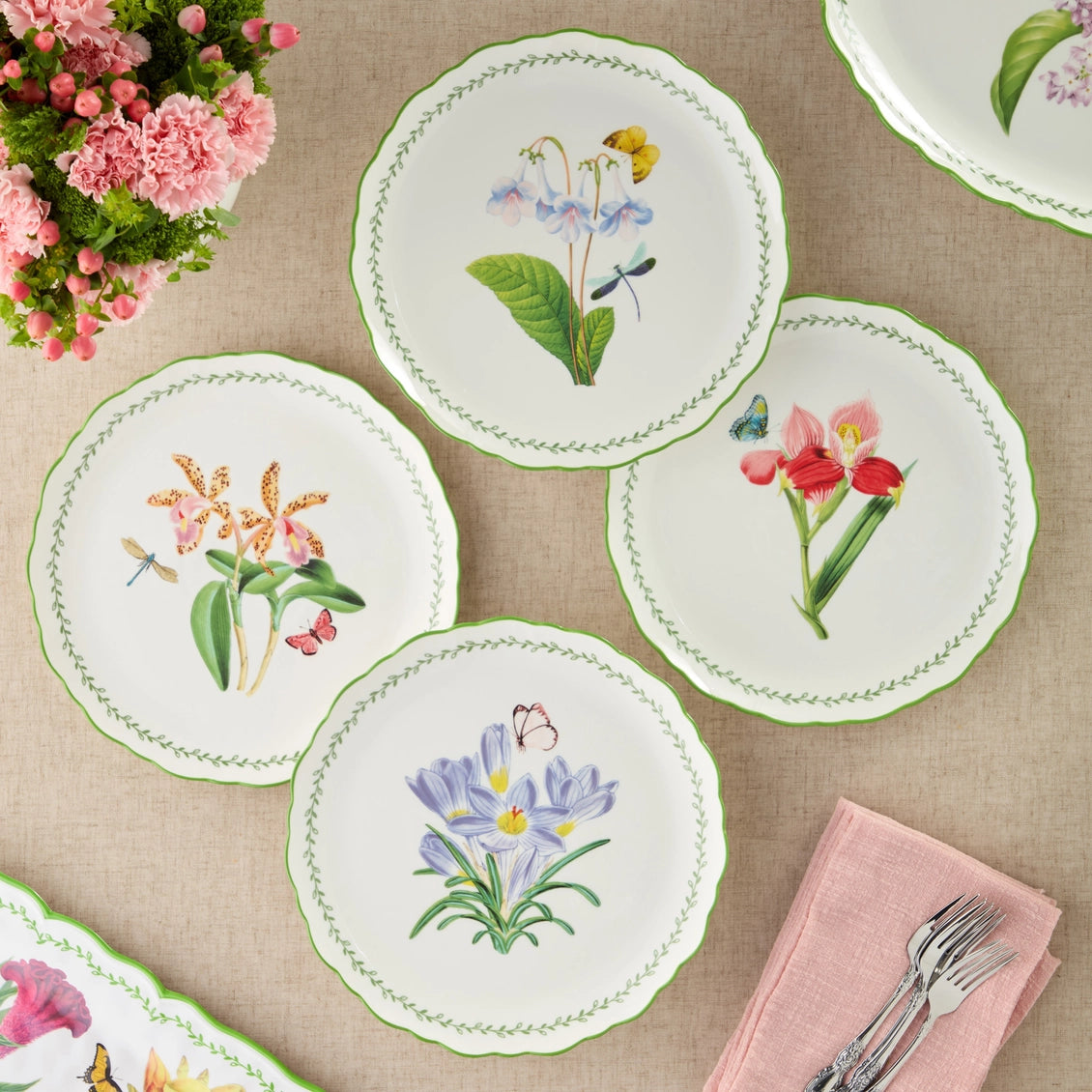 Set of floral embroidered plates on a tablecloth with pink flowers and cutlery.
