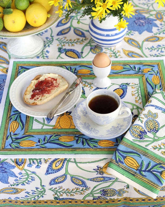 Breakfast setting on a colorful tablecloth with a cup of coffee, bread with jam, and an egg.