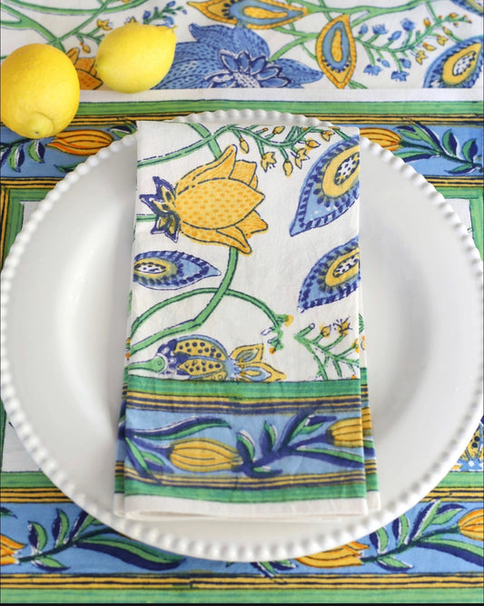 Decorative plate with a colorful floral pattern, lemons, and a matching napkin on a tablecloth.