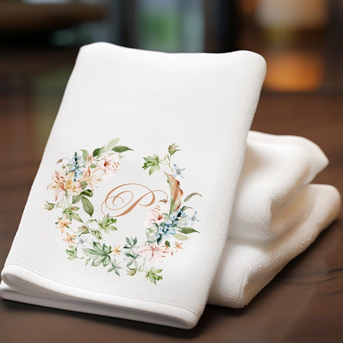 Folded white towel with floral design and letter 'P' on a wooden surface